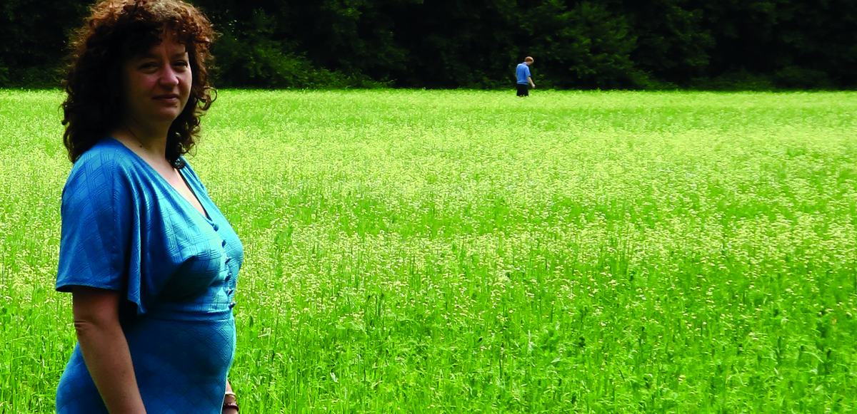 Een vrouw kijkt om in een bloeiend veld; op de achtergrond loopt een figuur weg.